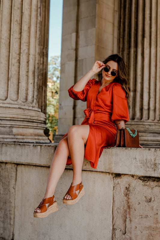 a woman sitting on a ledge with sandals and a red dress