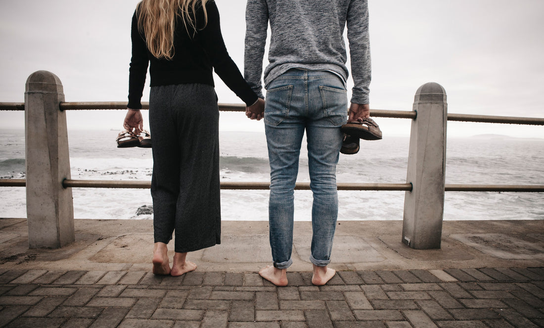 A couple looking at the ocean and holding hands and their Birkenstocks