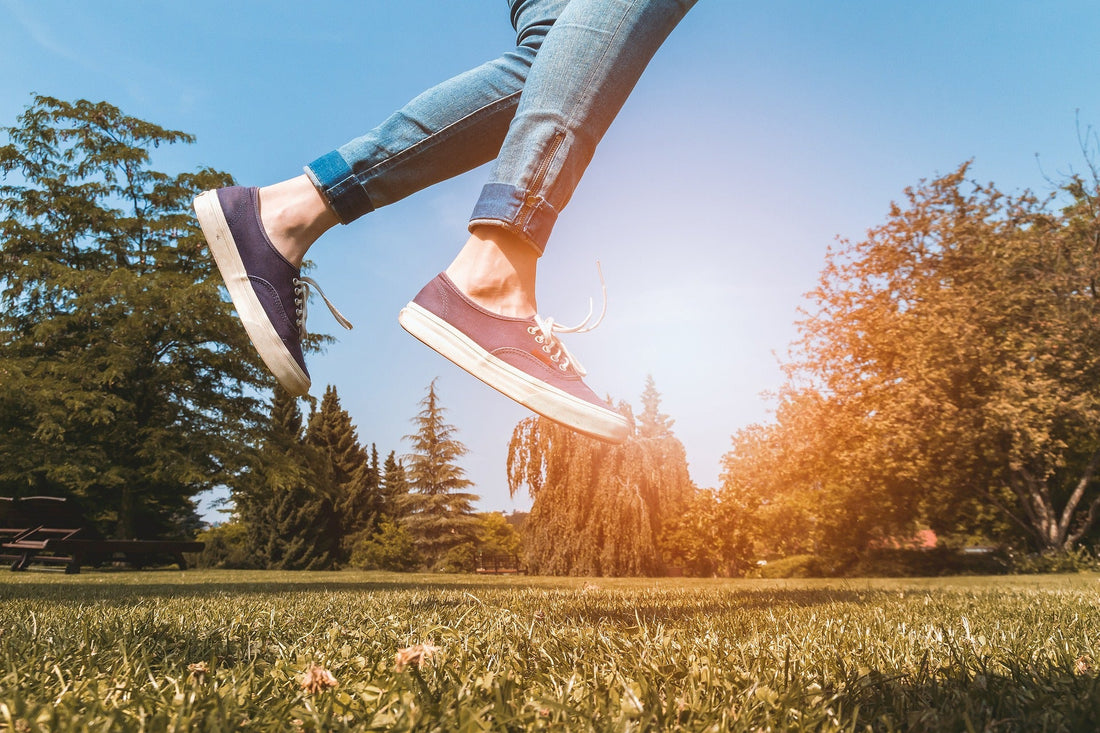 a woman wearing tennis shoes and jumping from the grass